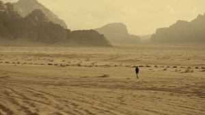 Person walking alone across a wide sandy desert under a cloudy sky